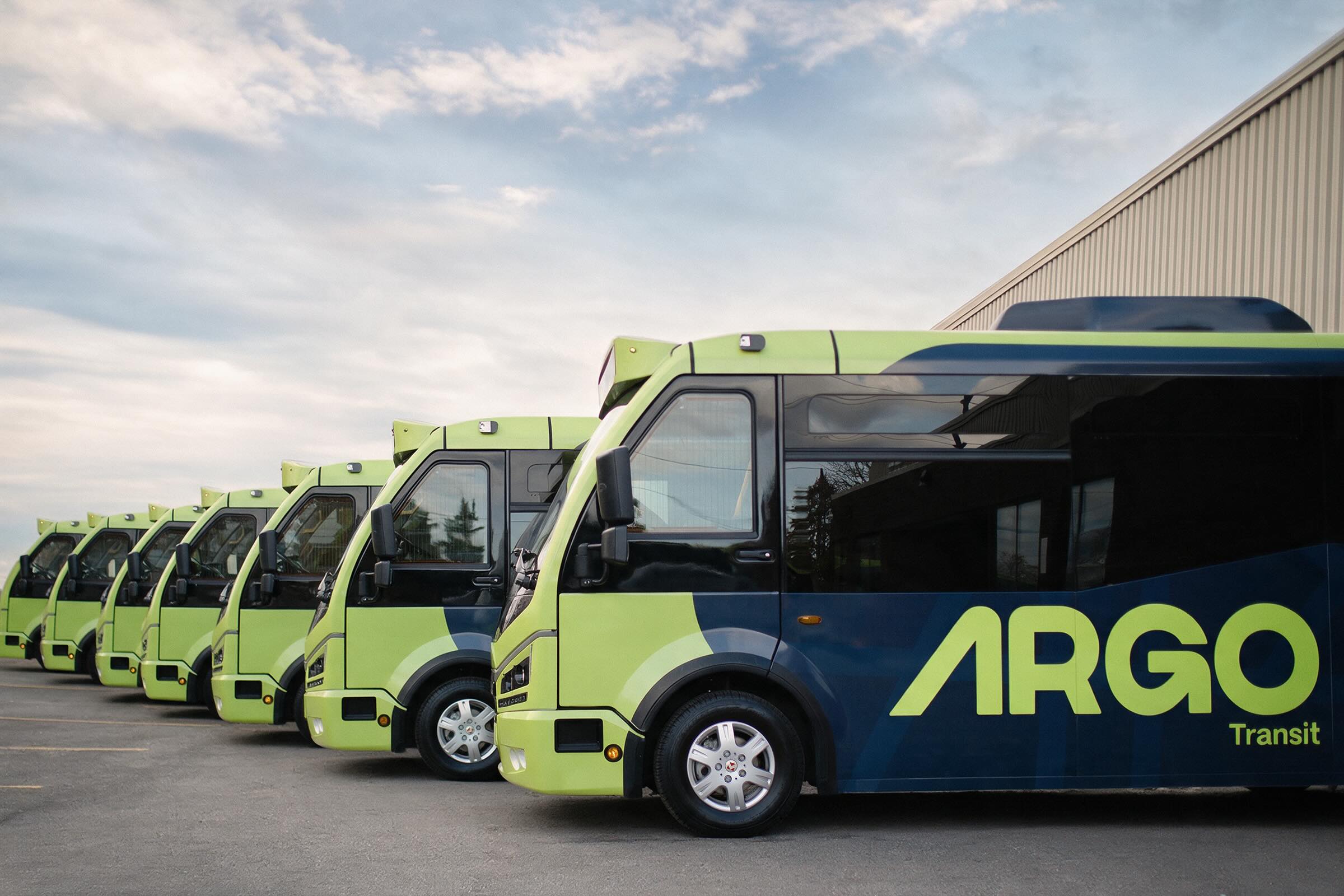 A row of fully electric Argo buses parked side by side in lime and navy livery
